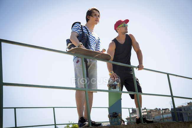Deux hommes, tenant des planches à roulettes, appuyés sur des balustrades — Photo de stock
