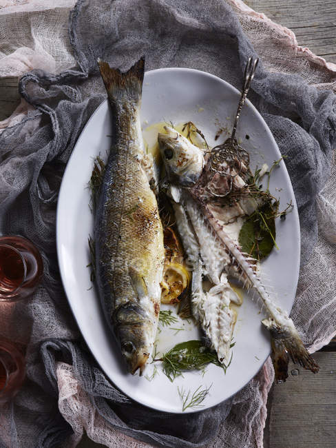 Top view of cooked branzino fish and bones on plate — Stock Photo