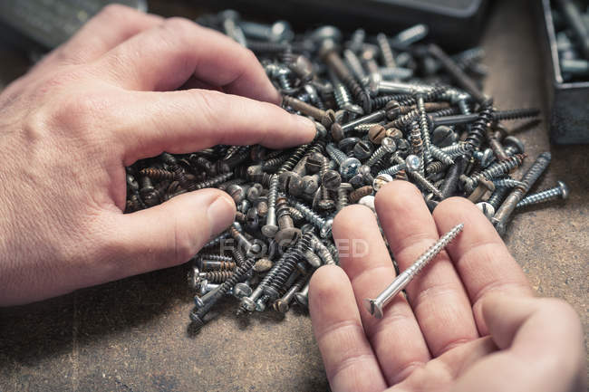 Paar Hände, eine Schraube, die aus einem Haufen unterschiedlich großer Schrauben herausragt — Stockfoto