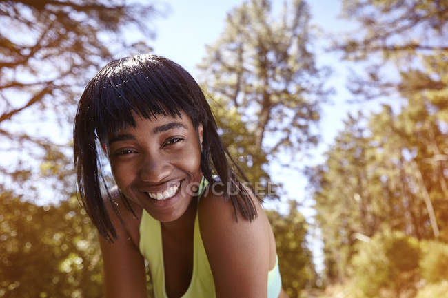 Porträt einer jungen Frau in ländlicher Umgebung, die sich in Richtung Kamera lehnt und lächelt — Stockfoto