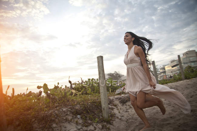 Mujer adulta corriendo a lo largo de pasarela arenosa hacia la playa - foto de stock
