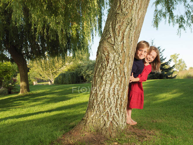 Niño y niña escondidos detrás del árbol - foto de stock