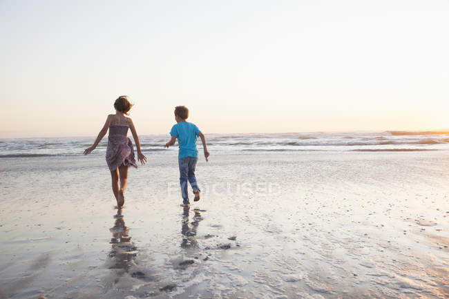 Vista trasera de hermano y hermana en la playa corriendo al océano - foto de stock