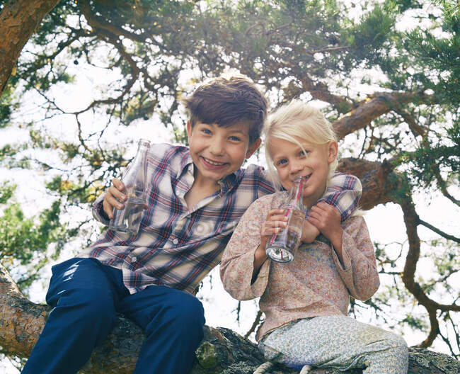 Due giovani amici seduti sull'albero, che bevono, sorridono — Foto stock