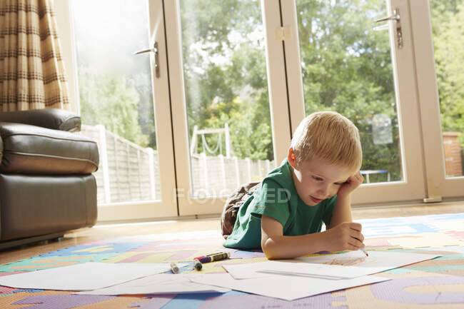 Хлопчик лежить на підлозі малює на папері — стокове фото