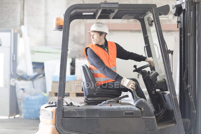 Jeune travailleur d'entrepôt inversant chariot élévateur dans l'entrepôt — Photo de stock