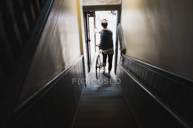 Young man at bottom of stairs, exiting building with bike, elevated view — Stock Photo