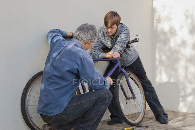 Отец помогает сыну ремонтировать велосипед — стоковое фото