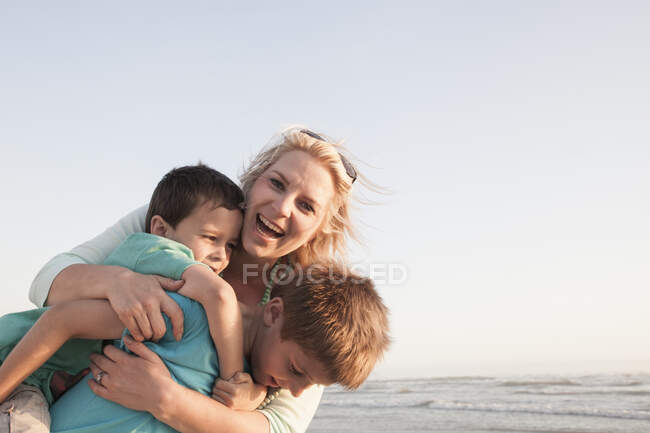 Mother by ocean hugging sons smiling — Stock Photo