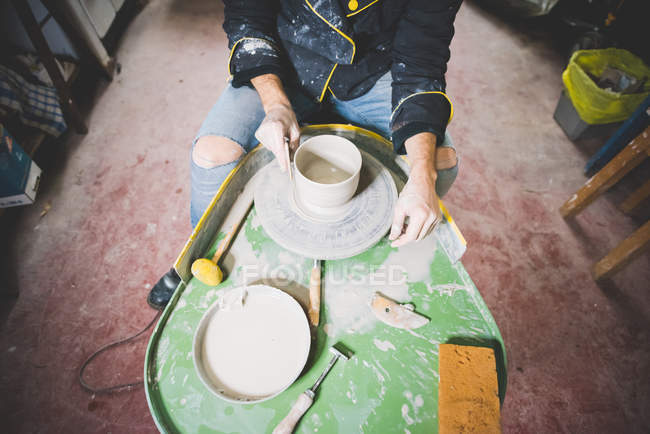 Vista de ángulo alto del hombre adulto medio haciendo olla de arcilla en la rueda de cerámica - foto de stock
