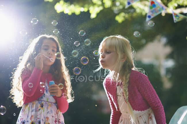 Duas meninas soprando bolhas no jardim iluminado pelo sol — Fotografia de Stock