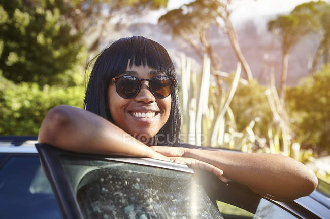 Portrait of young woman standing beside car, leaning on open car door — Stock Photo