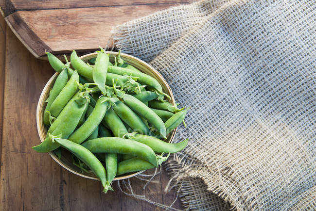 Bowl of green peas on table with burlap — Stock Photo
