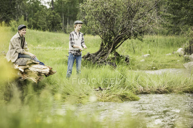 Brother and sister on riverbank fishing — Stock Photo
