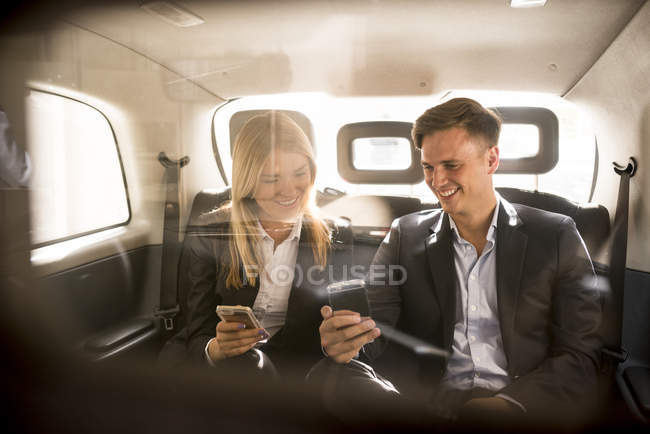 Businessman and businesswoman using smartphone in black cab, London, UK — Stock Photo