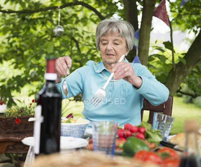 Mulher sênior servindo salada na mesa ao ar livre no jardim — Fotografia de Stock