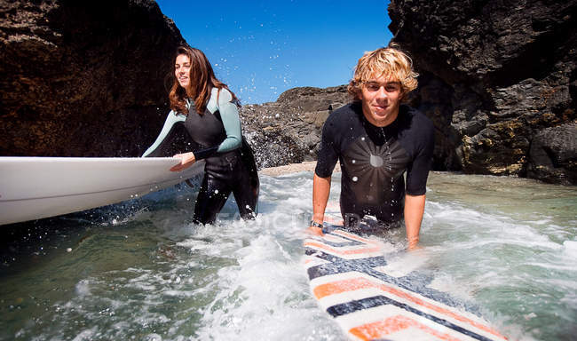 Pareja parada en el agua con tablas de surf - foto de stock