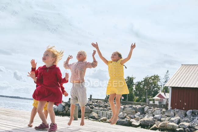 Group of young friends playing on wooden pier, reaching for bubbles — Stock Photo