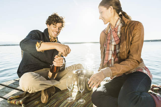 Coppia seduta in riva al lago con vino — Foto stock