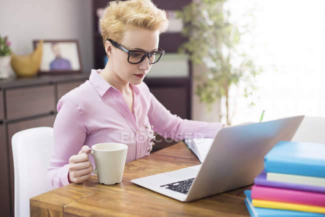 Femme utilisant un ordinateur portable et prenant un café au bureau — Photo de stock