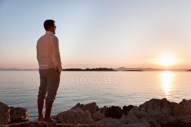 Чоловік спостерігає сонця кам'янистий пляж — стокове фото