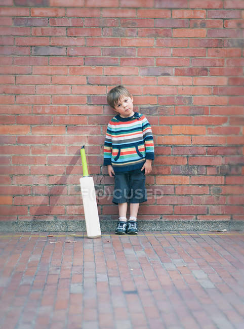 Мальчик с крикетной битой против кирпичной стены — стоковое фото