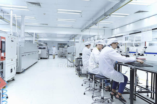 Male and female workers using microscopes in hi-tech factory — Stock Photo