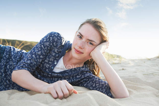 Teenager-Mädchen liegt auf Sand am Strand und blickt in Kamera — Stockfoto