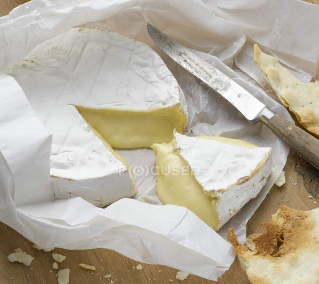 Sliced brie cheese on wrapping paper with knife — Stock Photo