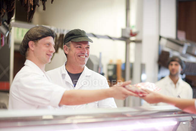 Men serving customer on butcher's counter — Stock Photo