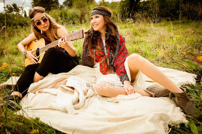 Хиппи молодых женщин на одеяле в поле, играющих на гитаре — стоковое фото