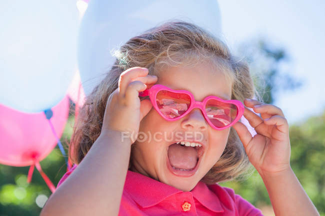 Fille portant des lunettes de soleil en forme de coeur rose — Photo de stock