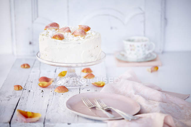 Natura morta di torta alla panna su bancarella guarnita con petali di rosa — Foto stock