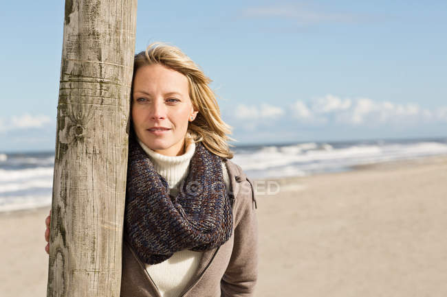 Woman leaning on pole on beach — Stock Photo