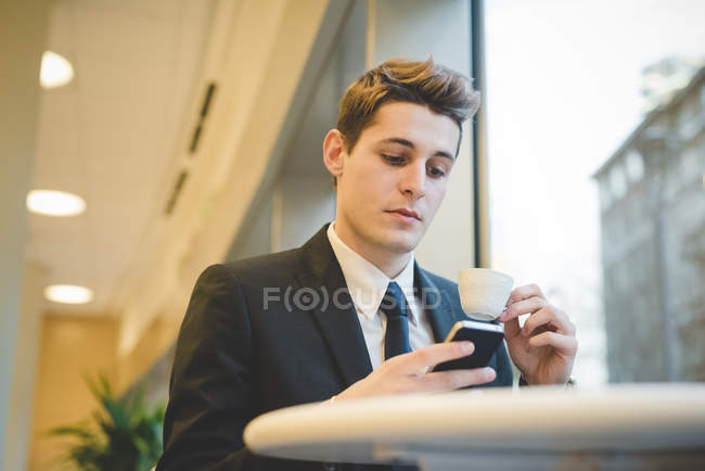 Portrait of young businessman sitting in cafe using digital tablet and mobile phone. — Stock Photo