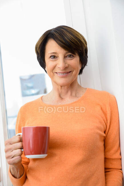 Жінка тримає чашку кави, посміхаючись — стокове фото
