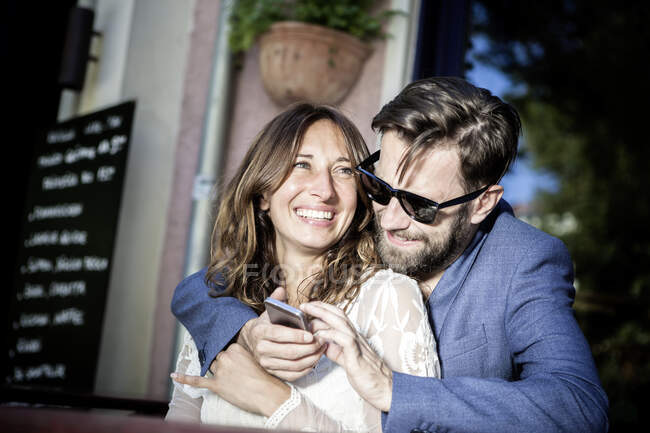 Coppia di abbracci e sorrisi, utilizzando smartphone, Berlino, Germania — Foto stock
