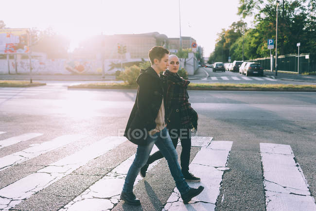 Young lesbian couple walking across pelican crossing city street — Stock Photo