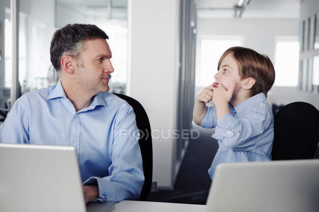 Padre usando laptop, hijo tirando caras - foto de stock