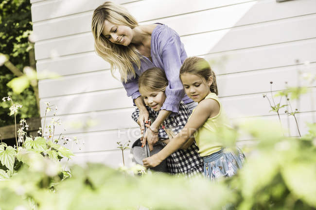 Mid adult woman and two daughters watering plants in garden — Stock Photo