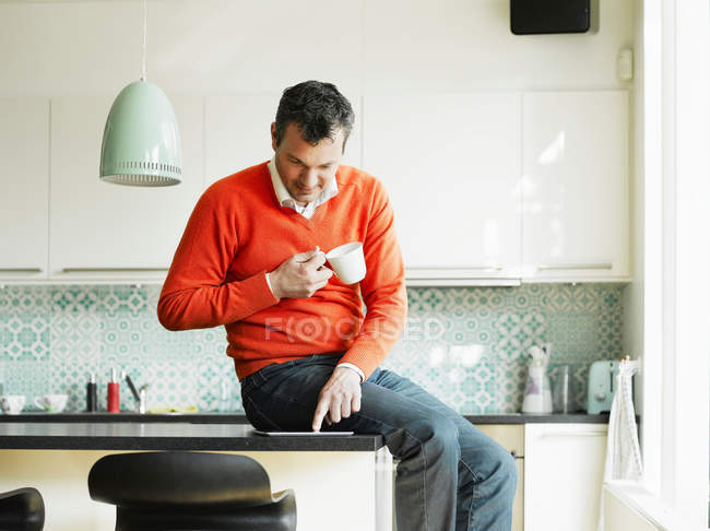 Чоловік використовує планшет і п'є каву на кухні — стокове фото