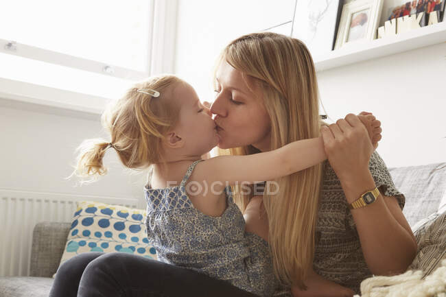 Доросла жінка цілує на дивані доньку - малюка. — стокове фото