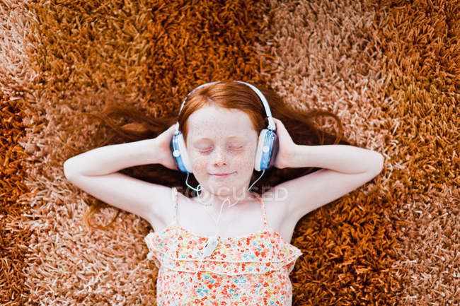 Girl listening to headphones on carpet — Stock Photo