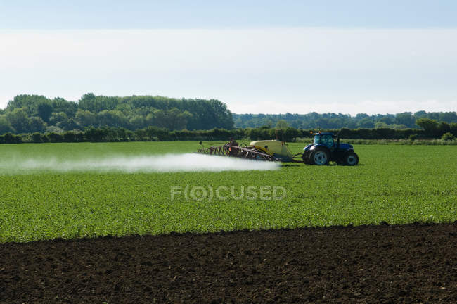 Tractor and crop sprayer spraying in countryside field — Stock Photo
