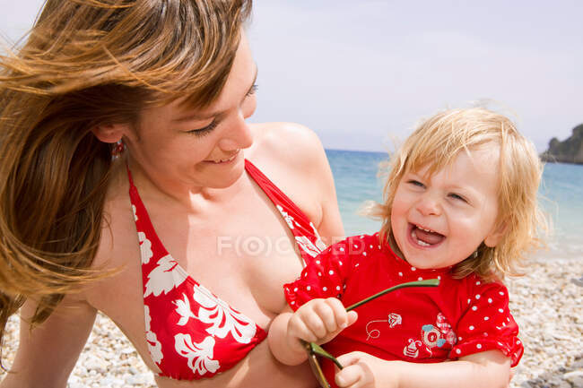 Madre e hija sonriendo en la playa - foto de stock
