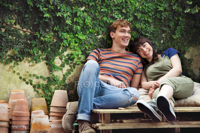 Couple sitting on wooden palettes beside plant pots — Stock Photo