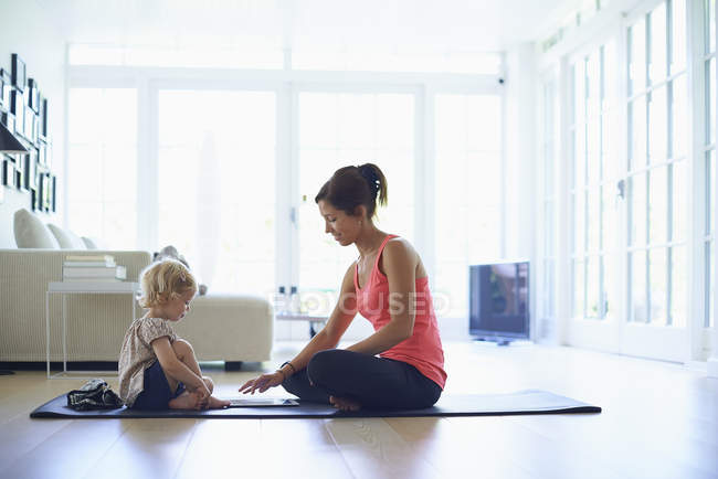 Madre adulta y hija pequeña practicando yoga en la sala de estar - foto de stock