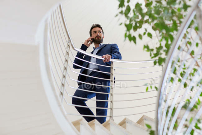 Молодой бизнесмен разговаривает по смартфону на офисной лестнице — стоковое фото