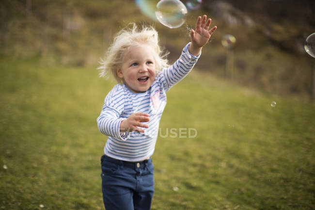 Chico persiguiendo burbujas, sonriendo - foto de stock