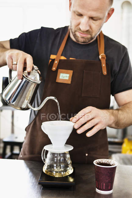 Male barista pouring boiling water into coffee filter — Stock Photo